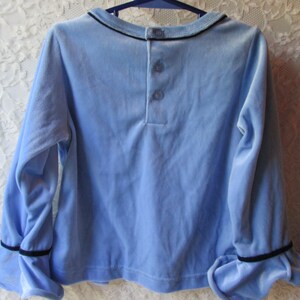 May include: A light blue long-sleeved shirt with black trim on the cuffs and collar. The shirt has three buttons on the back.