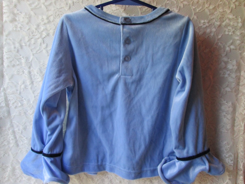 May include: A light blue long-sleeved shirt with black trim on the cuffs and collar. The shirt has three buttons on the back.