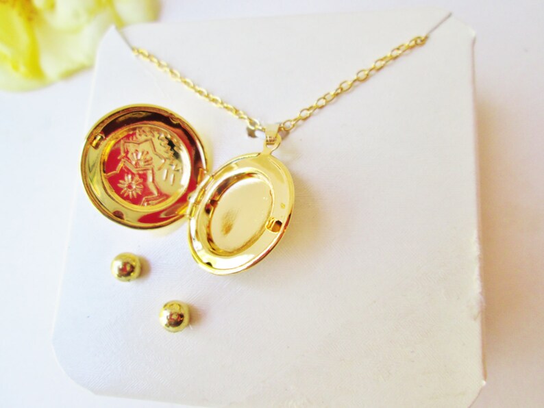 May include: Gold locket necklace with a small engraved design on the inside of the locket. The necklace comes with a pair of matching gold stud earrings.