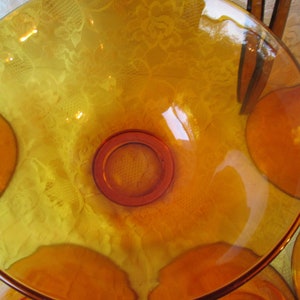 Peut inclure: Un saladier en verre ambr&eacute; avec un design large et peu profond. Le bol a une base circulaire et un bord l&eacute;g&egrave;rement sur&eacute;lev&eacute;. Plusieurs assiettes assorties sont visibles en arri&egrave;re-plan. Le verre a une teinte chaude et dor&eacute;e.