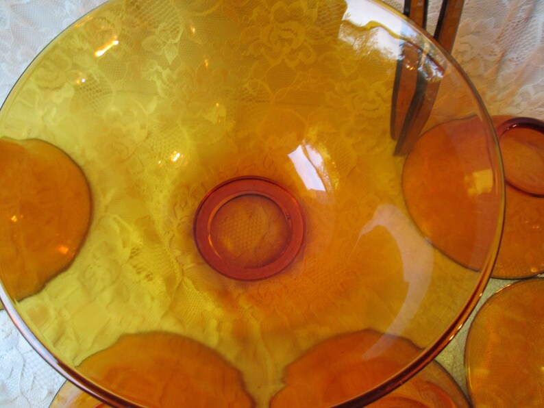 Peut inclure: Un saladier en verre ambr&eacute; avec un design large et peu profond. Le bol a une base circulaire et un bord l&eacute;g&egrave;rement sur&eacute;lev&eacute;. Plusieurs assiettes assorties sont visibles en arri&egrave;re-plan. Le verre a une teinte chaude et dor&eacute;e.