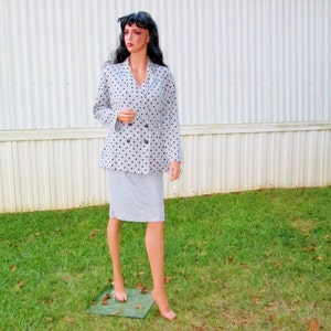 K&ouml;nnte beinhalten: Ein grauer und schwarzer Polka-Dot-Blazer mit doppelreihigem Verschluss und einem passenden Rock. Der Blazer hat lange &Auml;rmel und einen Kragen.
