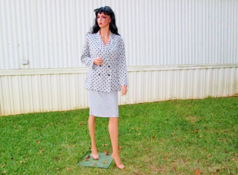 K&ouml;nnte beinhalten: Ein grauer und schwarzer Polka-Dot-Blazer mit doppelreihigem Verschluss und einem passenden Rock. Der Blazer hat lange &Auml;rmel und einen Kragen.