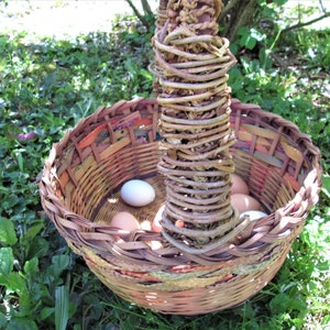 May include: A woven basket with a unique handle made of twisted branches. The basket is filled with brown and white eggs.