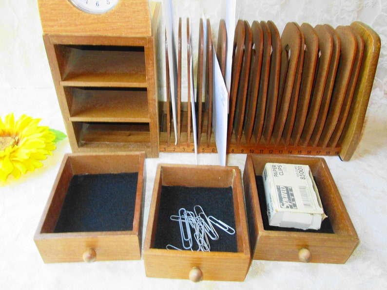 May include: Wooden desk organizer with a clock, letter slots, and three drawers. The drawers have black felt lining and one drawer contains paper clips. The top drawer has a wooden knob. The letter slots are numbered 3 to 18.