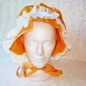 Puede incluir: Un gorro amarillo y blanco con ribete de volantes. El gorro est&aacute; hecho de sat&eacute;n y encaje.
