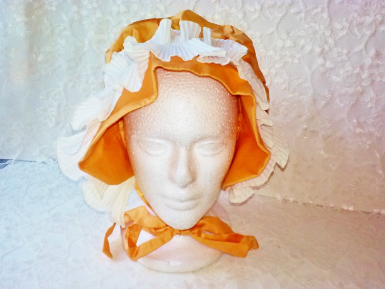 Puede incluir: Un gorro amarillo y blanco con ribete de volantes. El gorro est&aacute; hecho de sat&eacute;n y encaje.