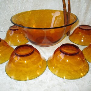 Peut inclure: Service &agrave; salade en verre ambr&eacute; comprenant un grand saladier avec un bord noir, six petits bols et des couverts. Les bols ont une finition textur&eacute;e et une couleur dor&eacute;e chaude. Parfait pour servir des salades ou d'autres plats.
