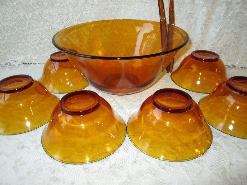 Peut inclure: Service &agrave; salade en verre ambr&eacute; comprenant un grand saladier avec un bord noir, six petits bols et des couverts. Les bols ont une finition textur&eacute;e et une couleur dor&eacute;e chaude. Parfait pour servir des salades ou d'autres plats.