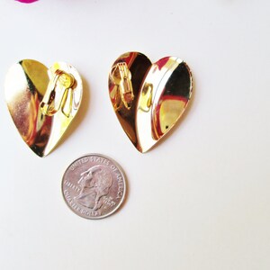 May include: A pair of gold heart-shaped clip-on earrings. The earrings are about the size of a quarter.