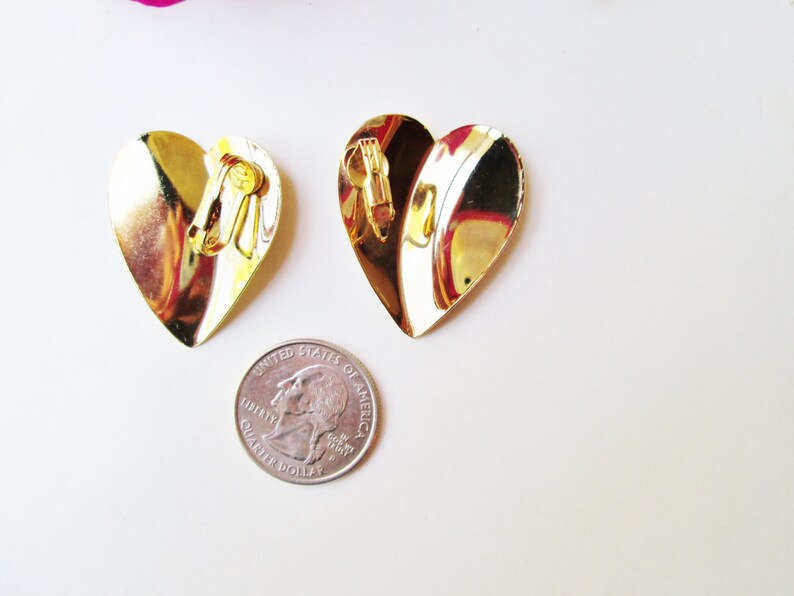May include: A pair of gold heart-shaped clip-on earrings. The earrings are about the size of a quarter.