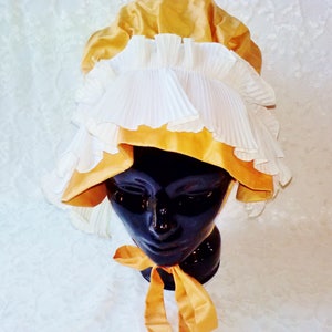 Puede incluir: Un gorro blanco y dorado con ribete de volantes. El gorro est&aacute; hecho de sat&eacute;n y encaje.