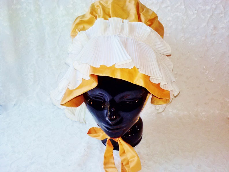 Puede incluir: Un gorro blanco y dorado con ribete de volantes. El gorro est&aacute; hecho de sat&eacute;n y encaje.