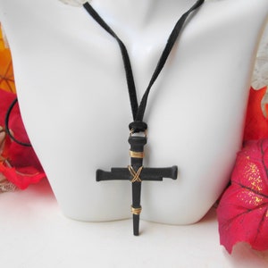 May include: A black nail cross pendant necklace with gold wire accents on a black suede cord.