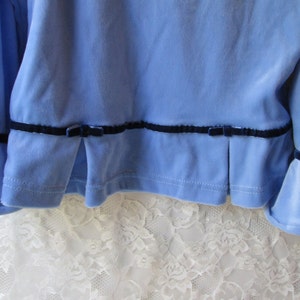 May include: A light blue velvet top with black velvet trim and bows at the bottom of the sleeves and hem.