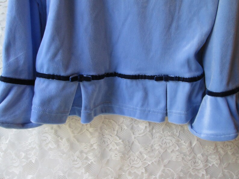 May include: A light blue velvet top with black velvet trim and bows at the bottom of the sleeves and hem.