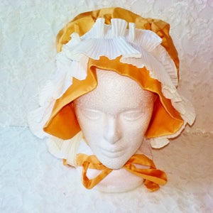 Puede incluir: Un gorro amarillo y blanco con ribete de volantes. El gorro est&aacute; hecho de sat&eacute;n y encaje.