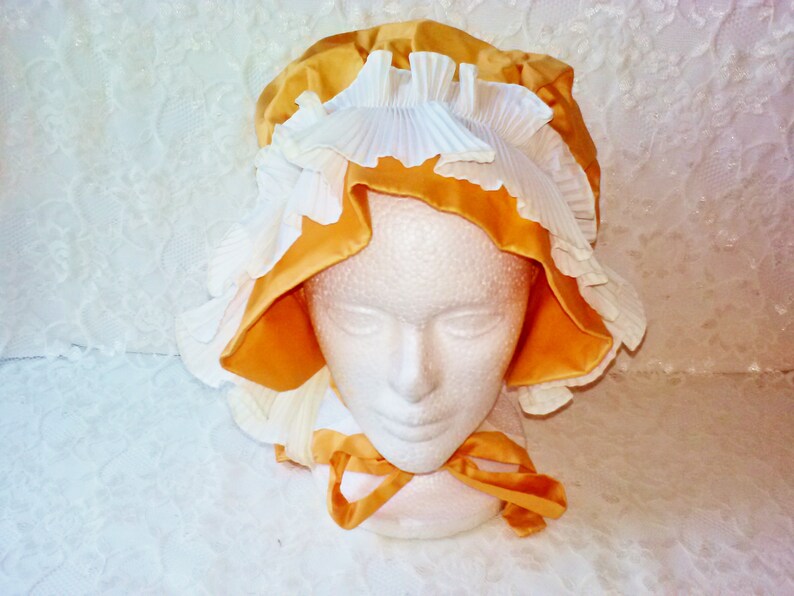 Puede incluir: Un gorro amarillo y blanco con ribete de volantes. El gorro est&aacute; hecho de sat&eacute;n y encaje.