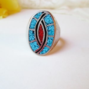 May include: A silver ring with an oval turquoise and red stone inlay. The ring has a geometric design with black lines.
