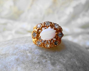 May include: A gold ring with a white oval stone surrounded by smaller clear stones.