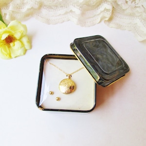 May include: A gold locket necklace and a pair of gold earrings in a black and white patterned gift box.