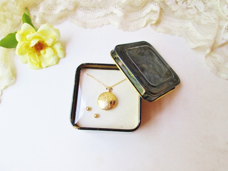 May include: A gold locket necklace and a pair of gold earrings in a black and white patterned gift box.