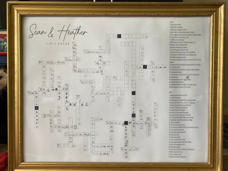 May include: A black and white crossword puzzle with the title "Sean & Heather Sip + Solve". The puzzle is framed in a gold frame.
