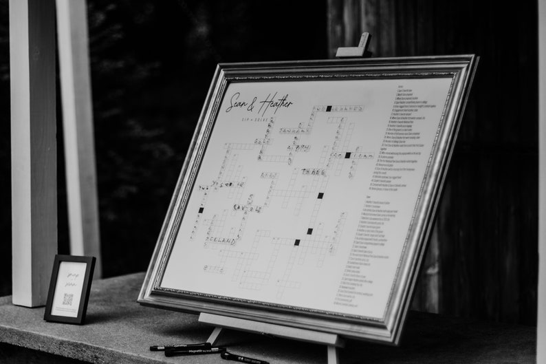 May include: A black and white photo of a wedding sign with a crossword puzzle. The sign says "Sean & Heather" at the top and has a list of clues for the crossword puzzle on the right side.