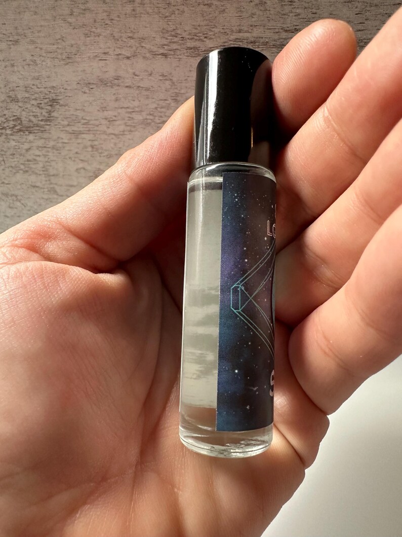 May include: A clear glass roller bottle with a black cap. The bottle has a label with a galaxy-themed design and the text "Love & Light" on it.