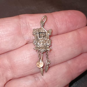 May include: Silver charm in the shape of a cuckoo clock with a detailed design and dangling chains.