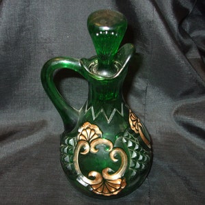 May include: A green glass bottle with a gold design. The bottle has a round body and a long neck with a stopper. The bottle is decorated with a gold floral pattern.