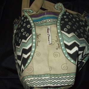 May include: A beige tote bag with a black, white, and green cat design. The bag has a brown handle and the text "Sweet Dreams" is printed on the front.