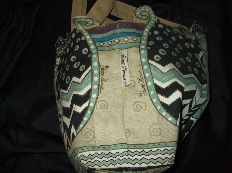 May include: A beige tote bag with a black, white, and green cat design. The bag has a brown handle and the text "Sweet Dreams" is printed on the front.