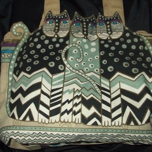 May include: A beige tote bag with a colorful design of three stylized cats. The cats are black, white, and green with gold accents. The bag has a geometric pattern and a whimsical design.