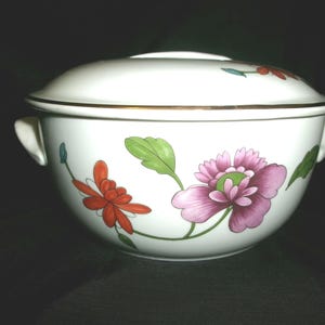 May include: White porcelain casserole dish with a lid, featuring a floral design with pink, red, and green flowers. The dish has a gold trim around the rim.