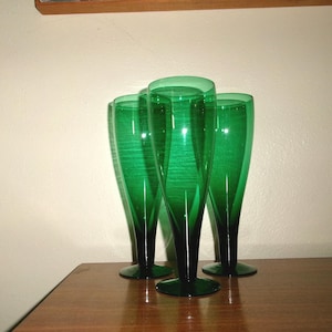 May include: Three tall, green glass champagne flutes with a dark green base.
