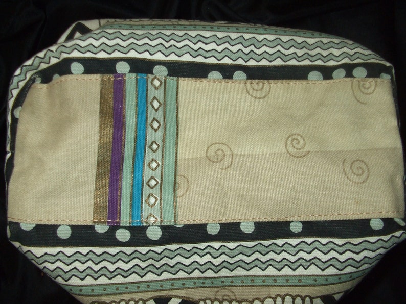 May include: A beige fabric tote bag with a black, white, and green geometric pattern. The bag has a large pocket on the front with a colorful striped design.