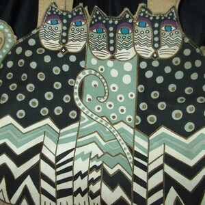 May include: A tote bag with a black, white, and green design featuring three stylized cats with large eyes and polka dots. The cats are arranged in a row with their tails intertwined. The bag has a brown leather handle.