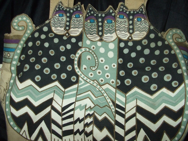 May include: A tote bag with a black, white, and green design featuring three stylized cats with large eyes and polka dots. The cats are arranged in a row with their tails intertwined. The bag has a brown leather handle.