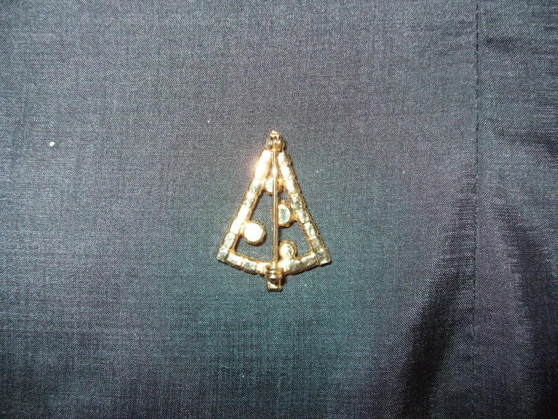 May include: A gold-toned Christmas tree brooch with clear rhinestones. The brooch is in the shape of a stylized Christmas tree with a pin on the back.