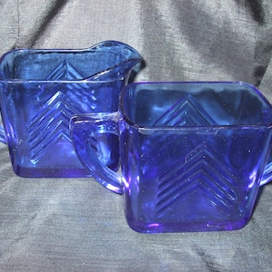 May include: A set of two cobalt blue glass creamer and sugar bowl with a geometric pattern.