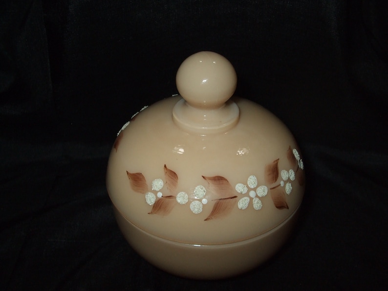 May include: A vintage glass jar with a lid, featuring a floral design in brown and white. The jar is a pale peach color.