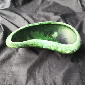 May include: A green ceramic planter shaped like a long, curved bean. The planter has a speckled, textured surface.