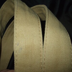 May include: Close-up of two beige canvas straps sewn together. The straps are thick and have a woven texture.