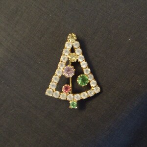 May include: A gold-tone Christmas tree brooch with clear, pink, green, and purple rhinestones.