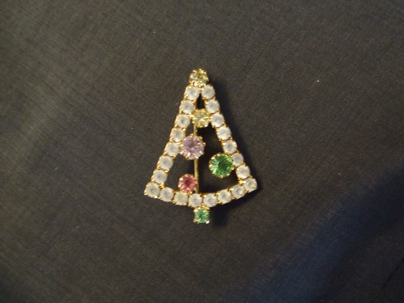 May include: A gold-tone Christmas tree brooch with clear, pink, green, and purple rhinestones.