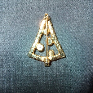 May include: Gold-tone Christmas tree brooch with clear rhinestones. The brooch is in the shape of a triangle and has a pin back.