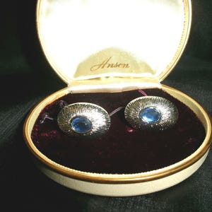 May include: A pair of silver cufflinks with blue glass stones in a velvet lined box with the word "Anson" printed on the lid.