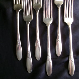 May include: Set of six silver forks with ornate handles. The forks are laid out on a black surface.