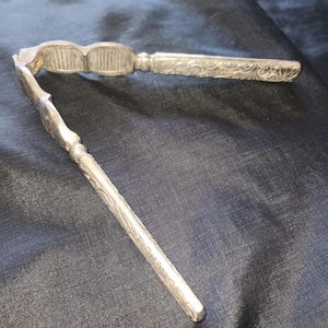 May include: A silver nutcracker with an ornate design. The nutcracker is open and ready to crack nuts.